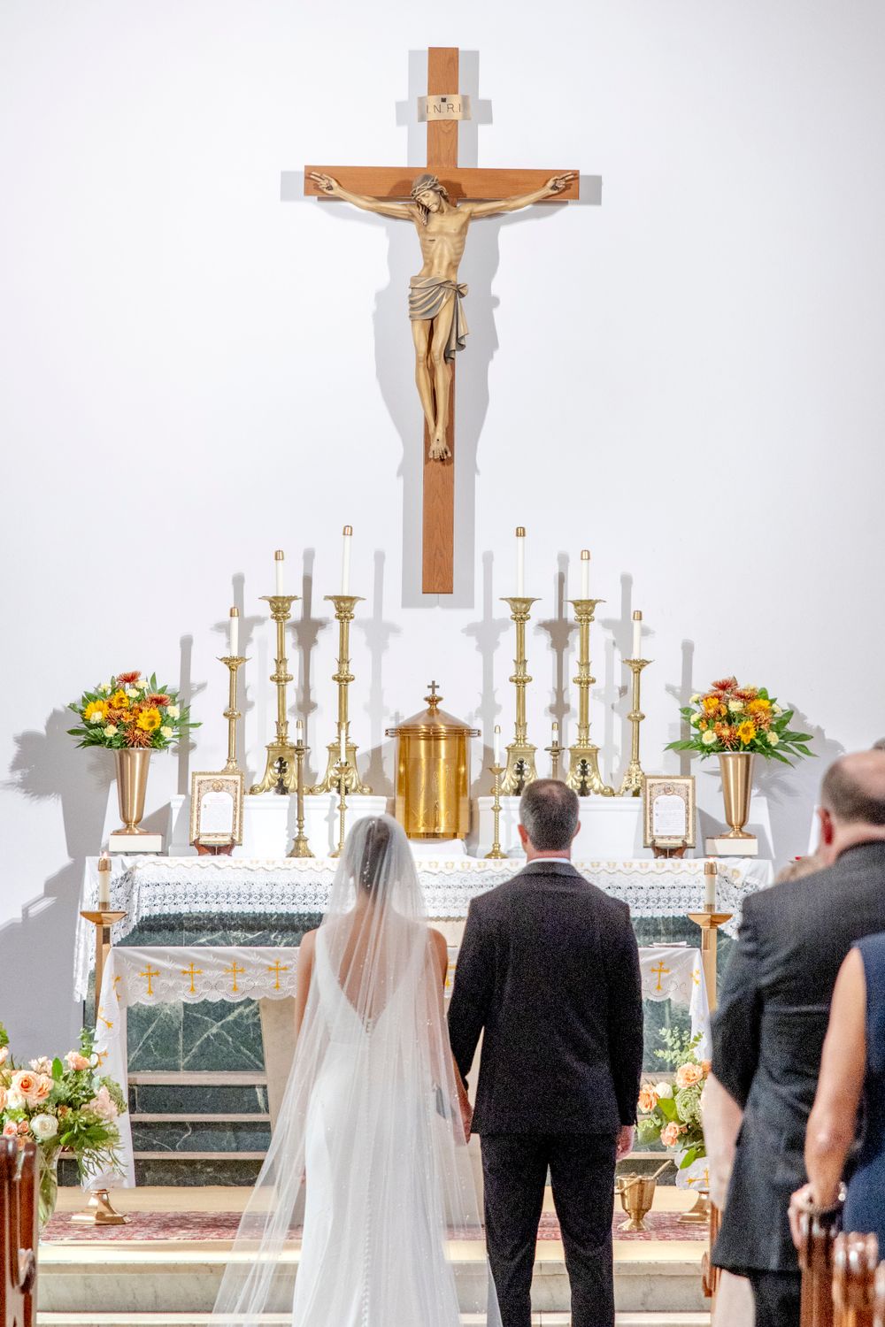 Church altar adorned with golden candlesticks, floral arrangements, and a large crucifix during a wedding ceremony.
