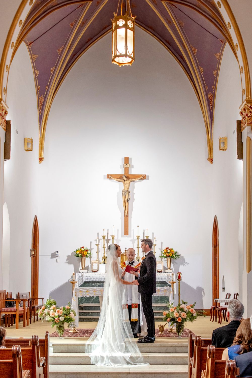Catholic church wedding ceremony under gothic arches with golden accents and hanging lanterns.