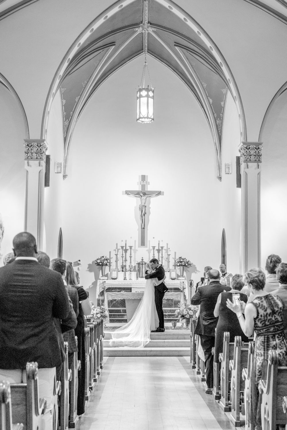 Black and white view down church aisle showing vaulted ceiling and gathered wedding guests.