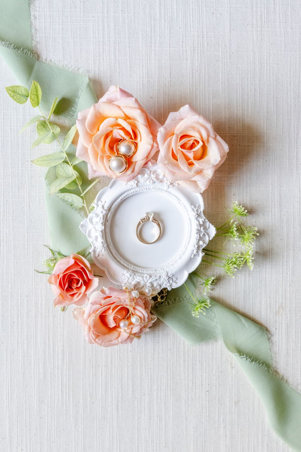 Engagement ring displayed on ornate white dish surrounded by peach roses and mint green ribbon.