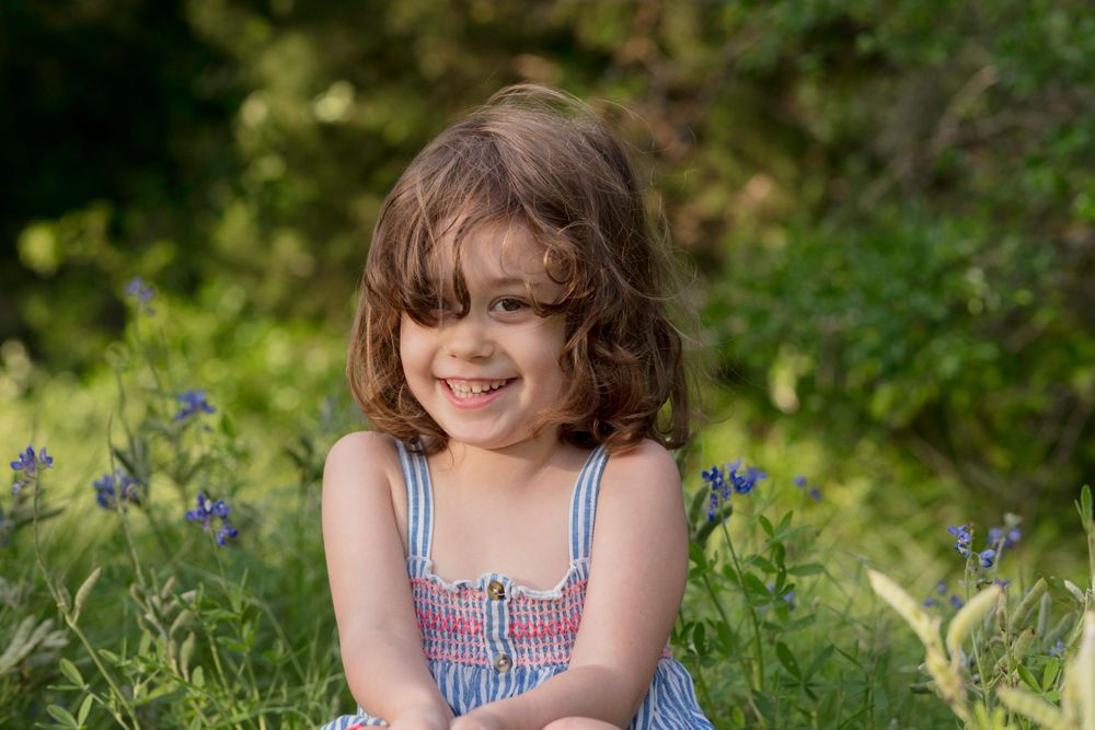 Curly haired girl sits in spring field smiling. Bluebonnet Mini Session