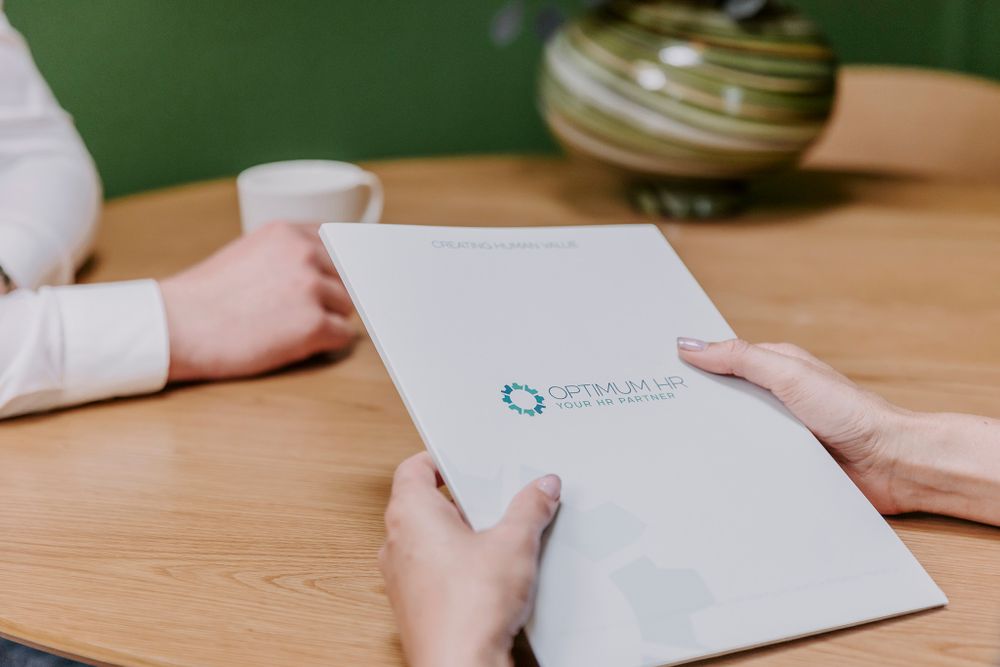 Nærbillede af hænder, der holder forretningsdokumenter med Optimum HR Partner-branding. Branding fotograf Fyn.