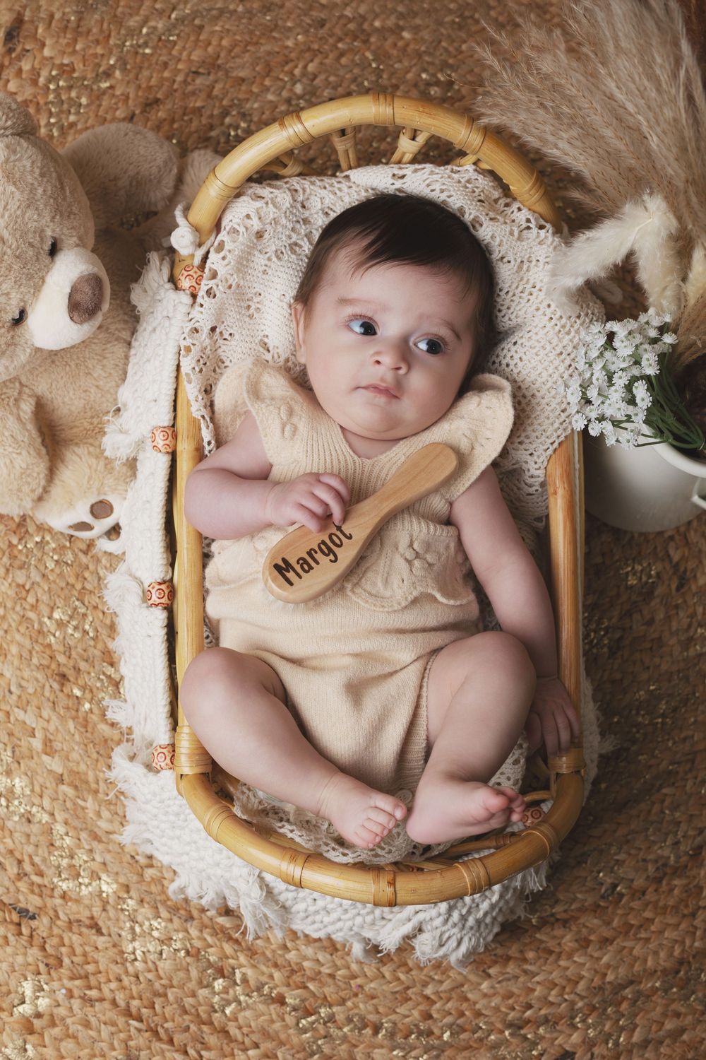 Newborn baby named Margot lying in a wicker basket with a wooden brush, teddy bear, and white flowers.
