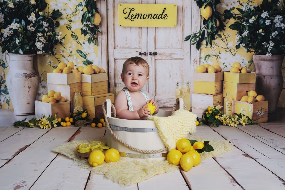 Yellow lemonade stand photo backdrop with rustic wood floors, lemons, and yellow flowers for baby photography.