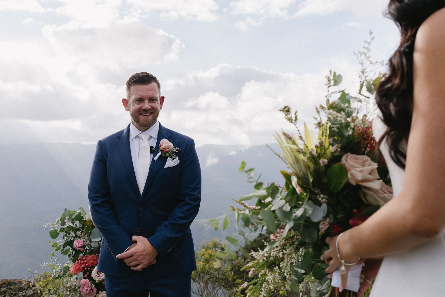 A wedding ceremony on a scenic mountain overlook with cloudy skies and natural greenery.