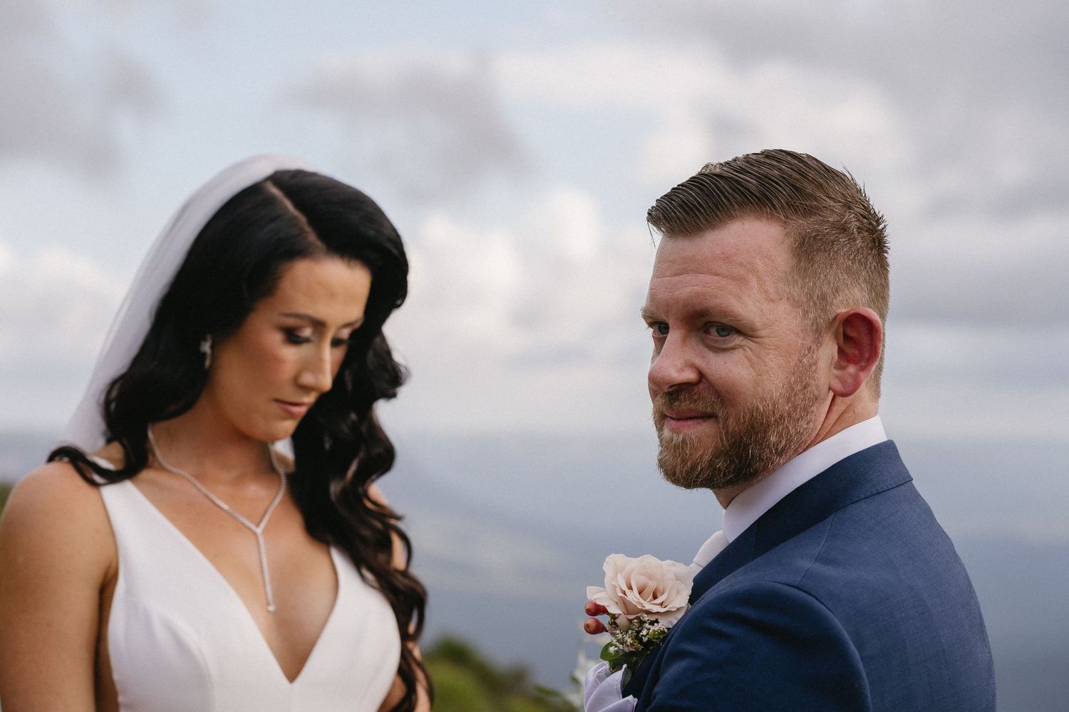 Close-up outdoor wedding portrait with cloudy mountain backdrop.