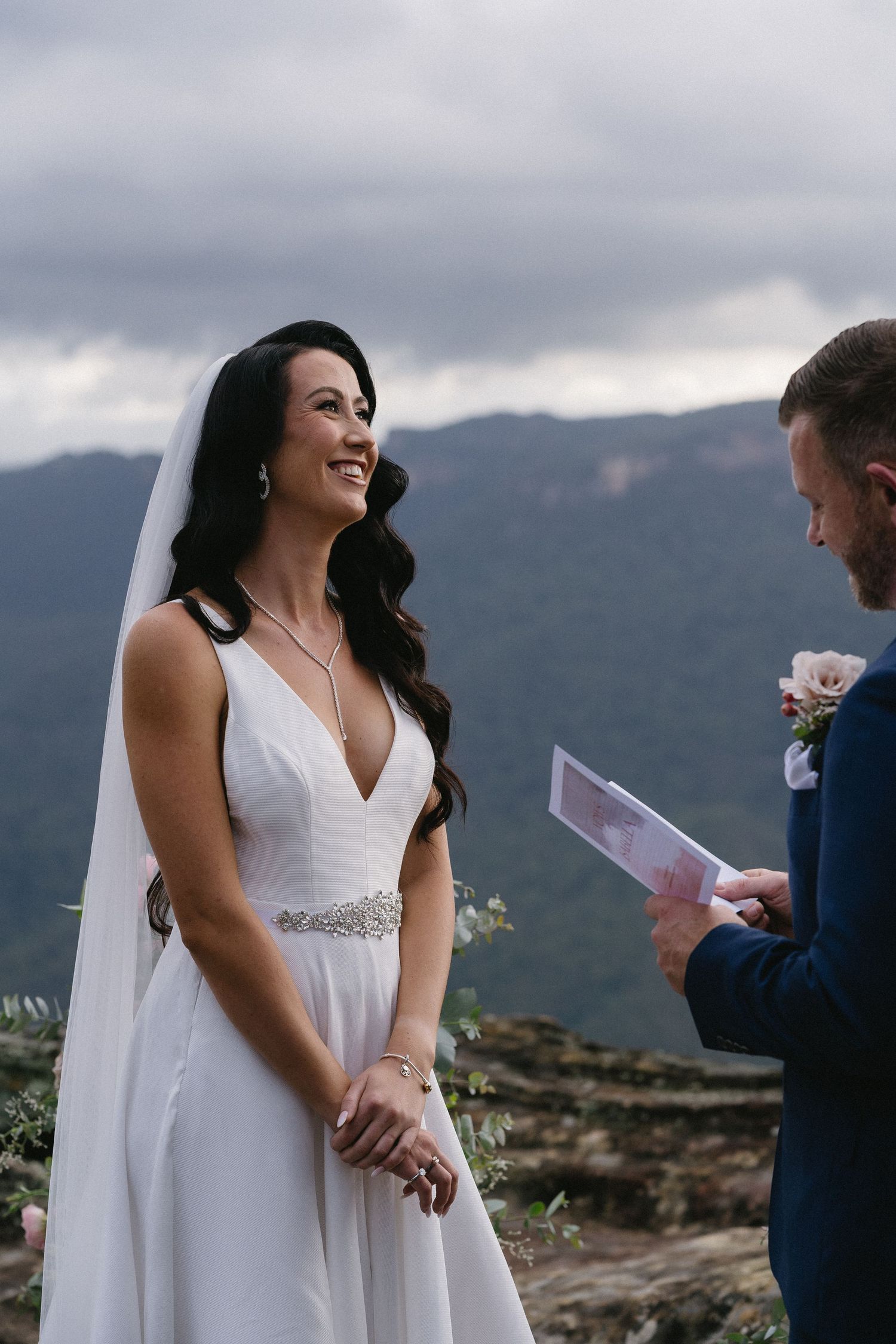 Wedding ceremony moment on mountain overlook with dramatic cloudy sky background.