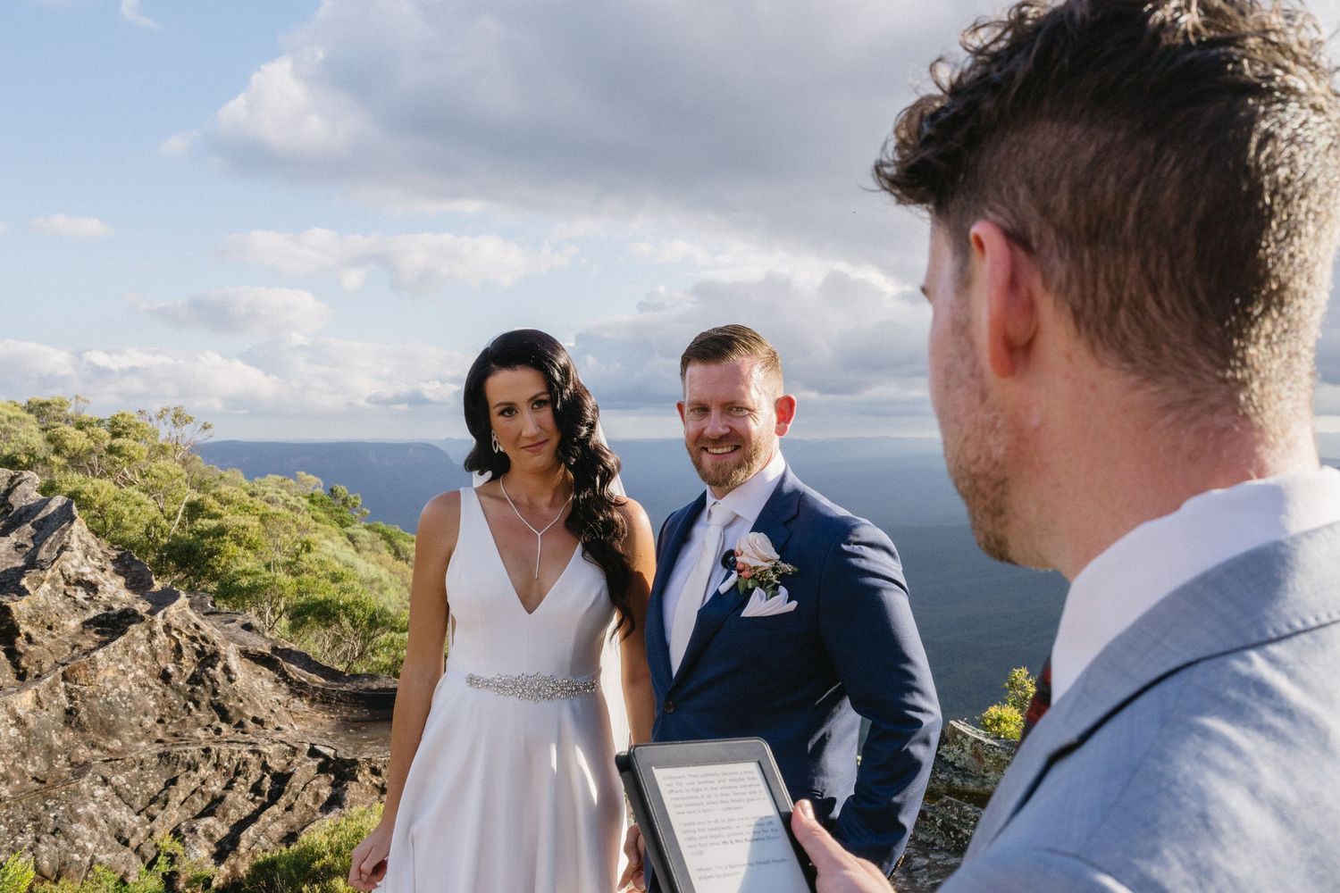 Two people share an intimate outdoor wedding ceremony moment atop a scenic cliff overlooking the valley