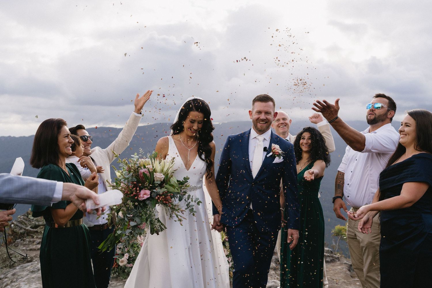 Joyous wedding celebration with confetti toss against mountainous backdrop.
