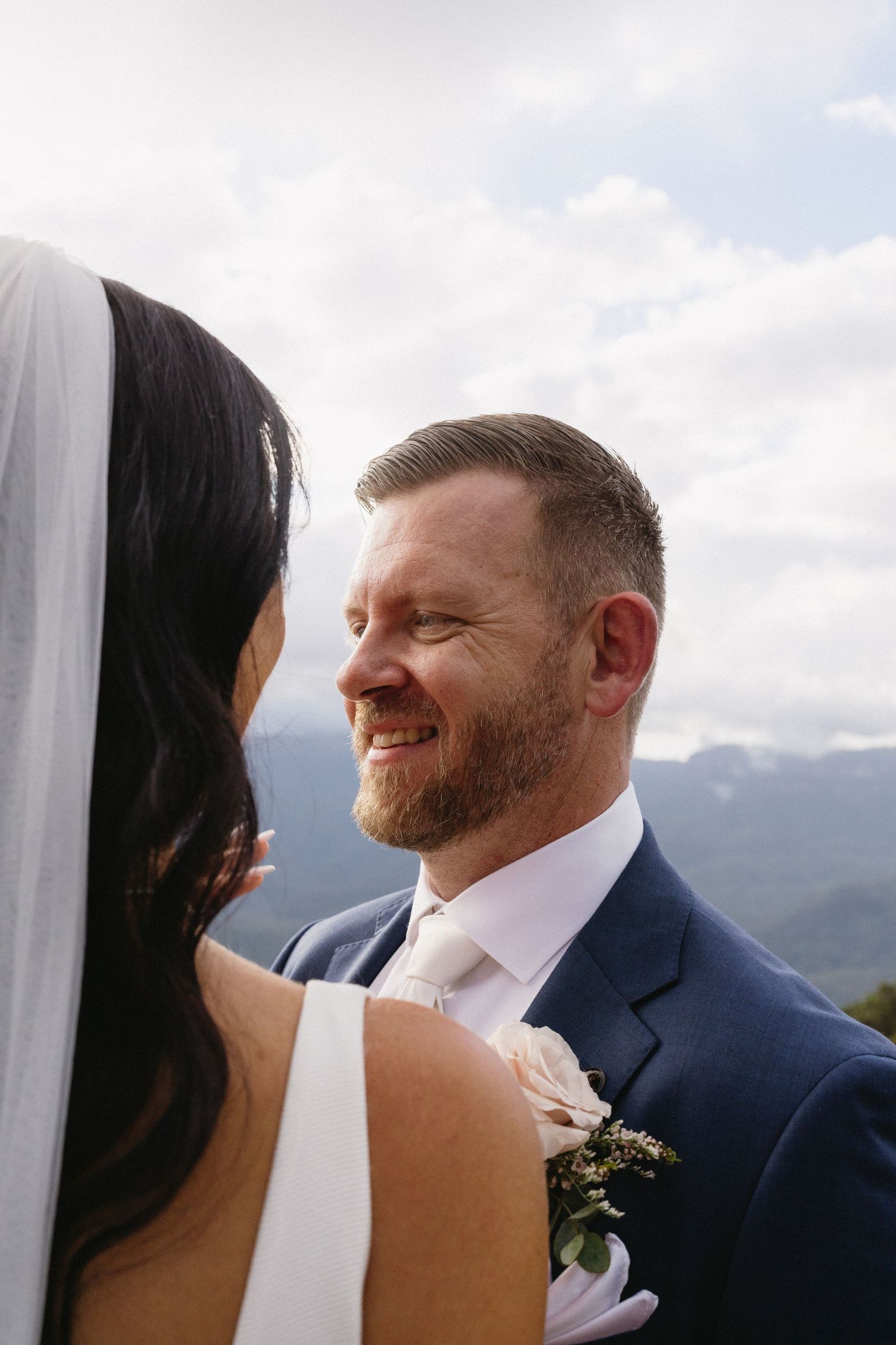 Intimate wedding moment captured against mountain scenery and cloudy skies.
