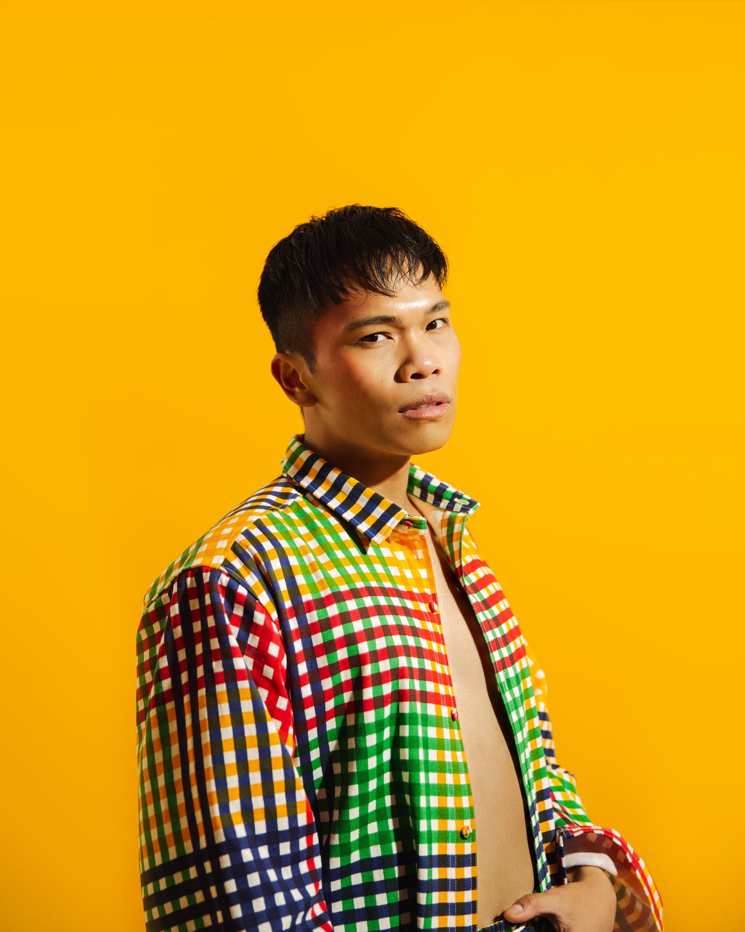A person wearing a colorful checkered pattern shirt poses against a vibrant yellow background.