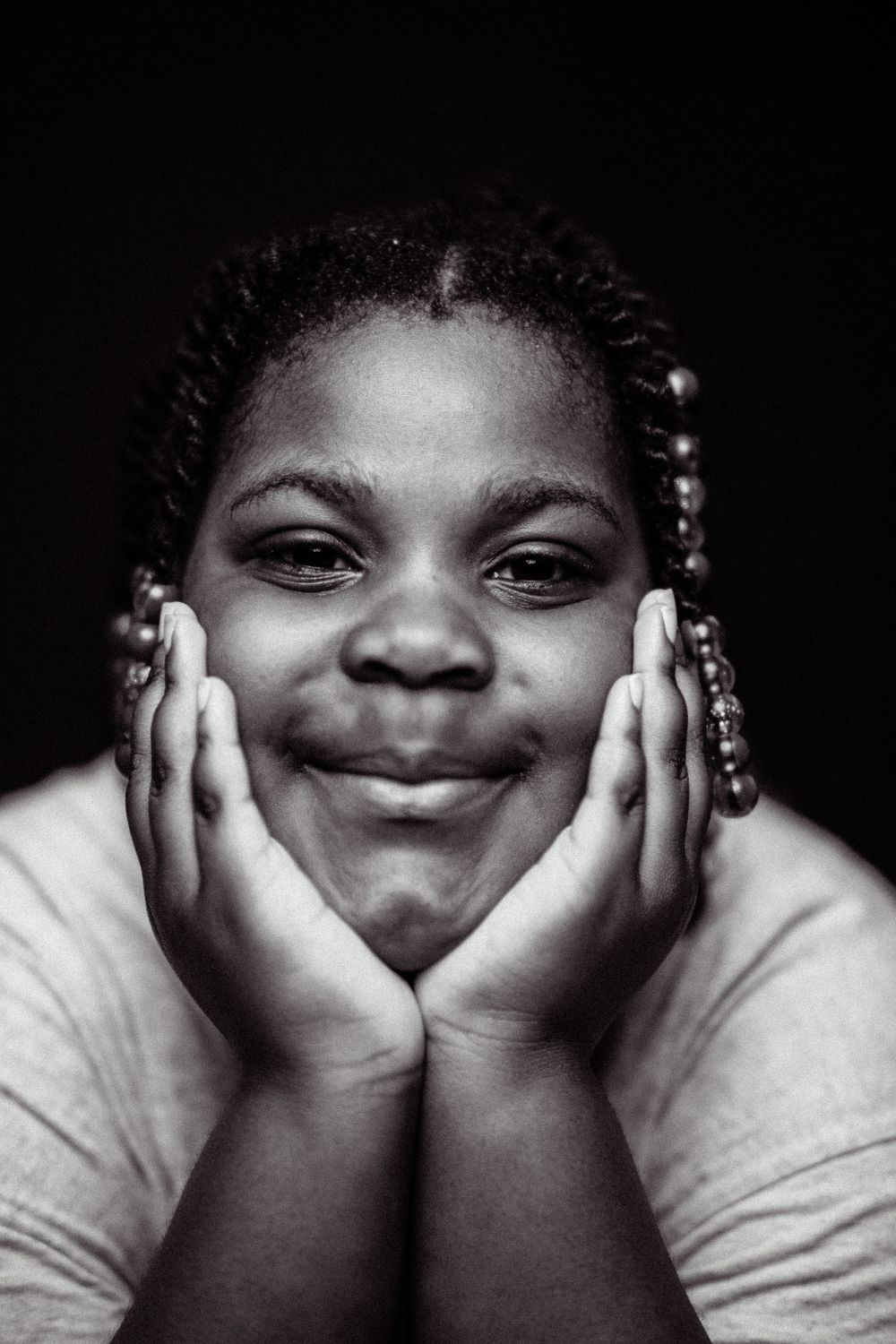 Black and white portrait with gentle expression and braided hair against dark background.