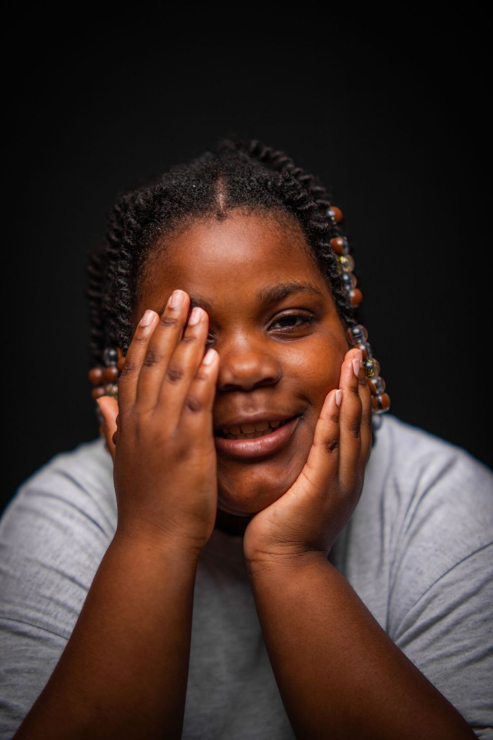 Expressive portrait with hands framing face against dark background.