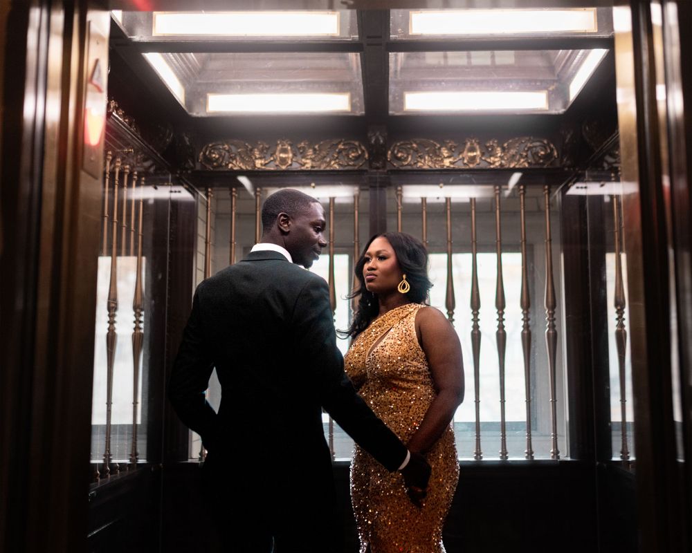 Silhouetted couple shares intimate moment in ornate corridor with backlit windows.