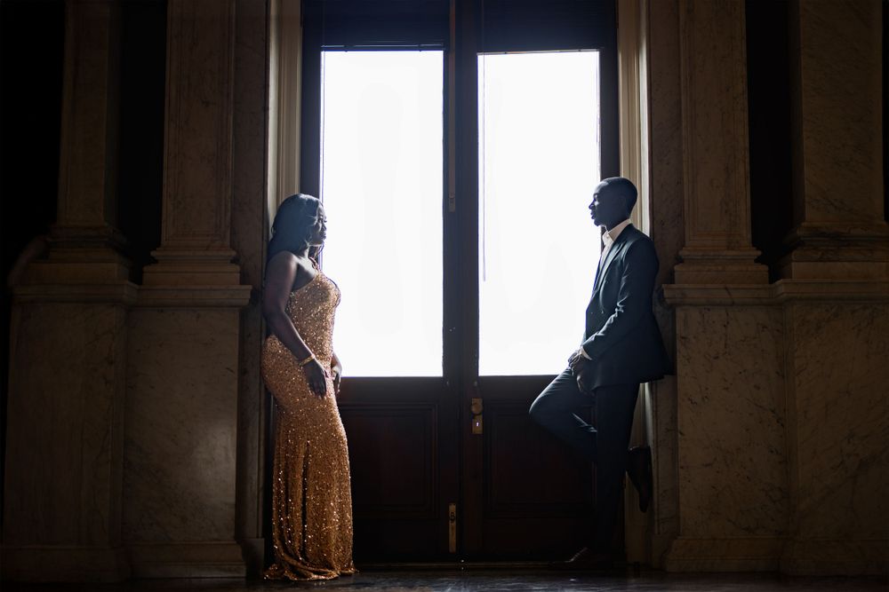 Dramatic silhouette of couple by large windows in architectural setting.
