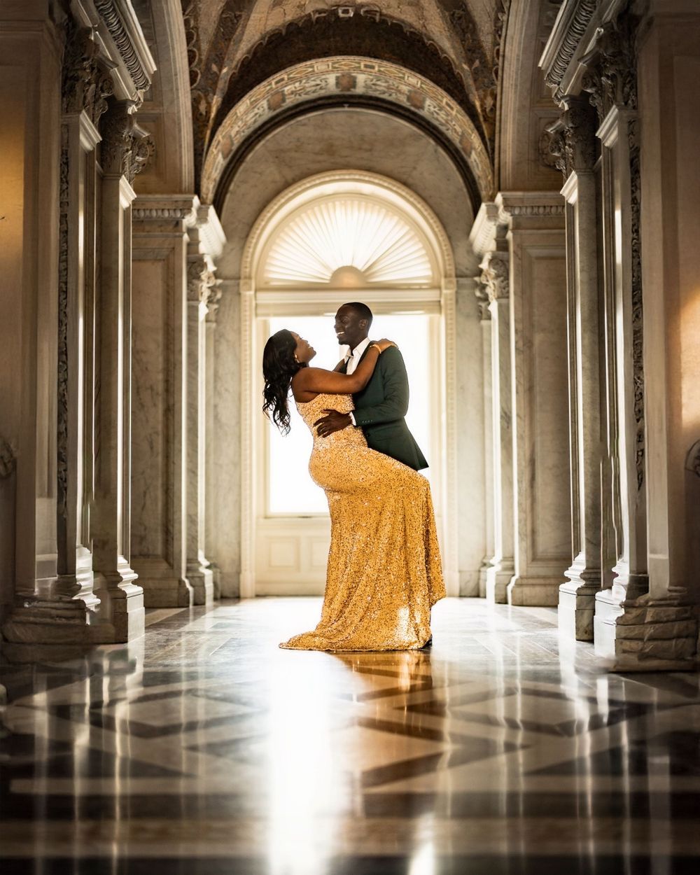 Couple in formal wear dances in elegant hallway with arched columns and dramatic lighting.