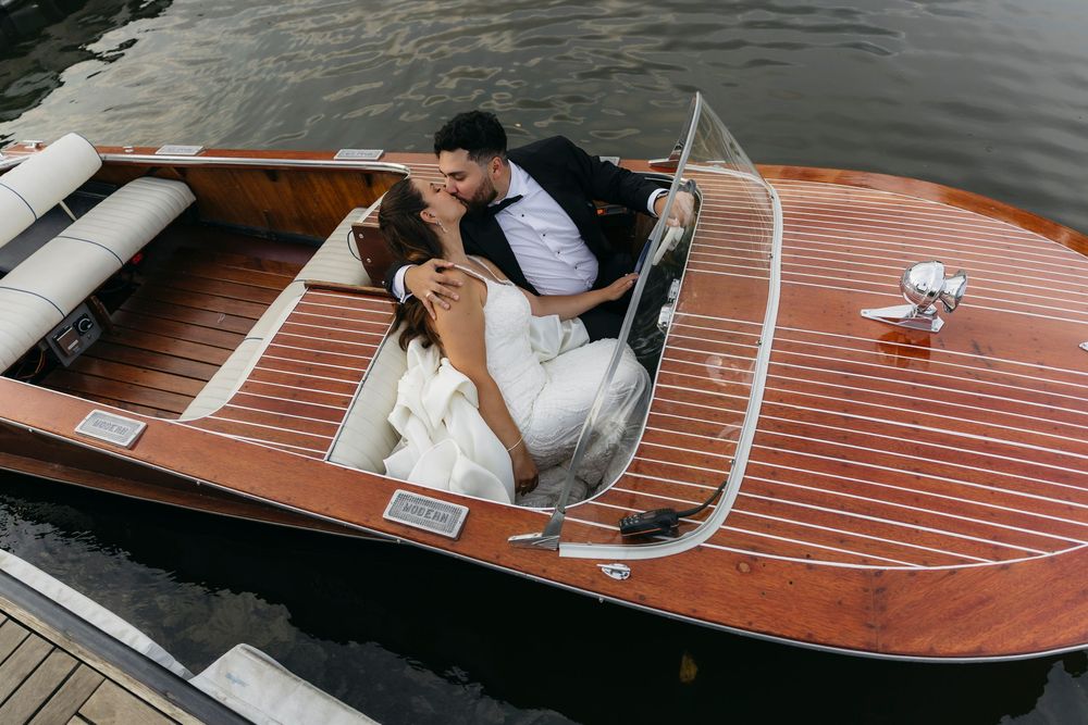 Classic wooden boat with teak deck glides across rippling water on a sunny day.