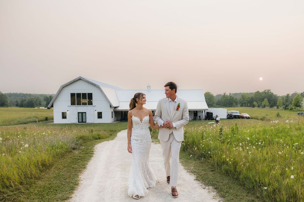Wedding couple walking through a wildflower field with white barn in background.