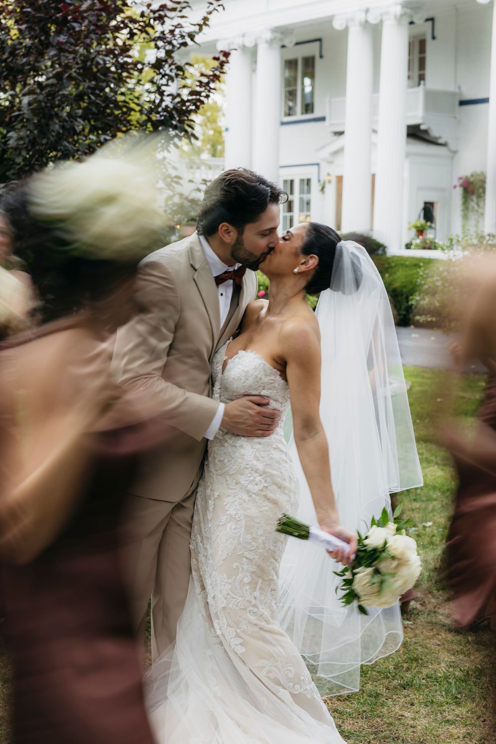 Romantic wedding moment captured in front of a white colonial style house with garden landscaping.