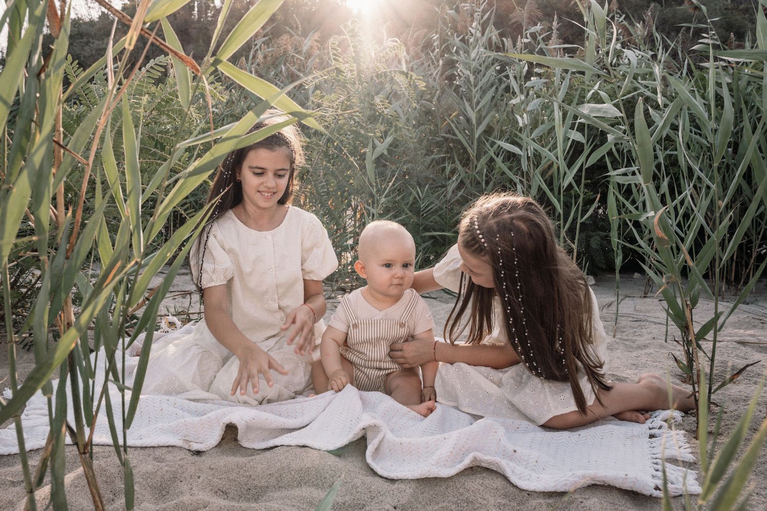 Family sitting on blanket among tall grass during golden hour photoshoot.