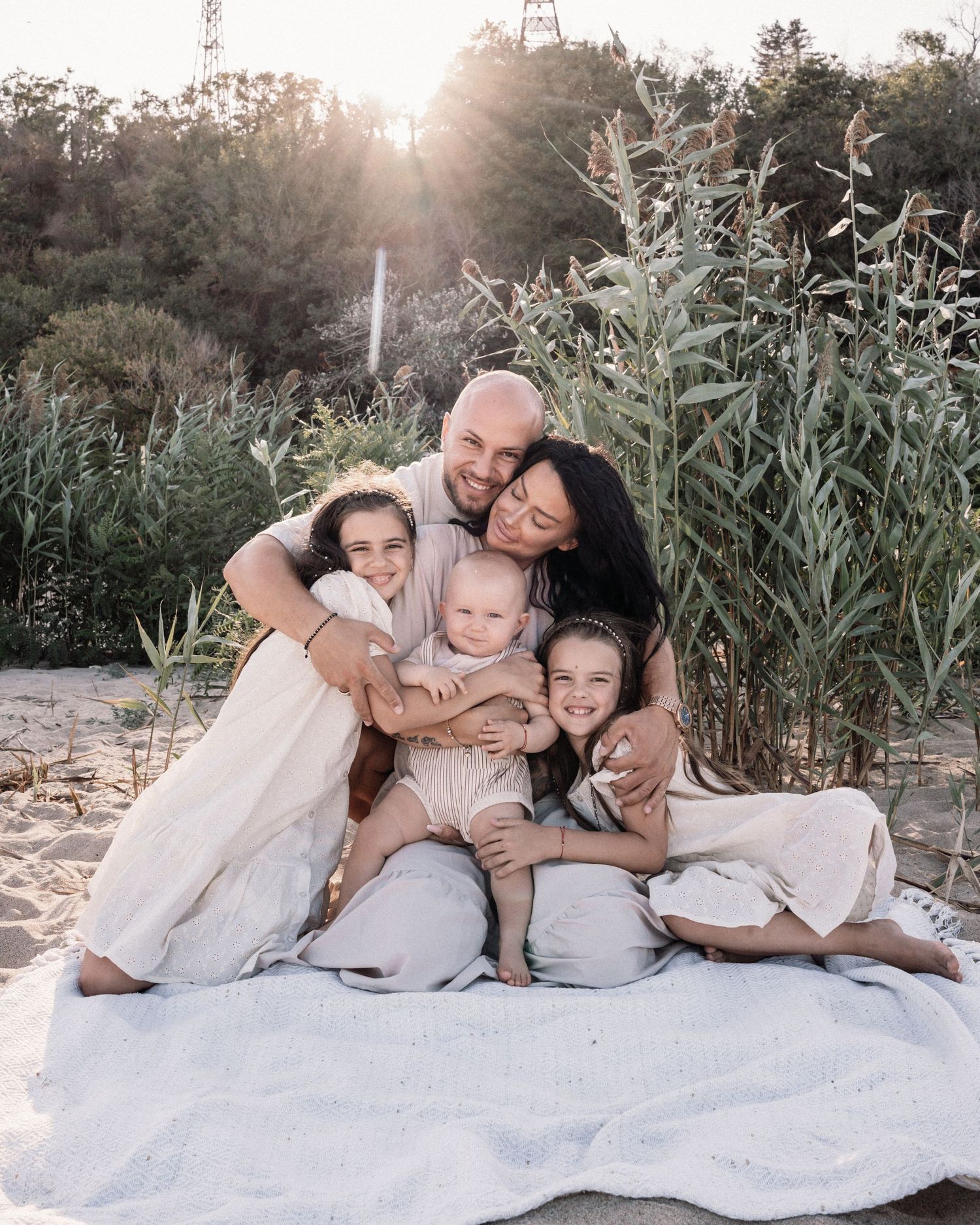 Family of five cuddling together on white blanket during outdoor photoshoot.
