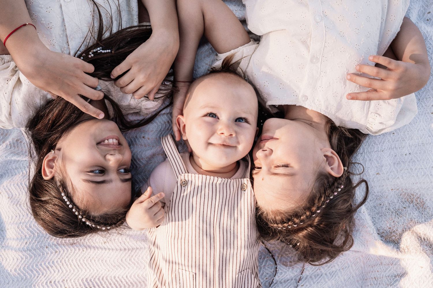 Family members lie on sand while looking up at camera in coordinated white outfits.