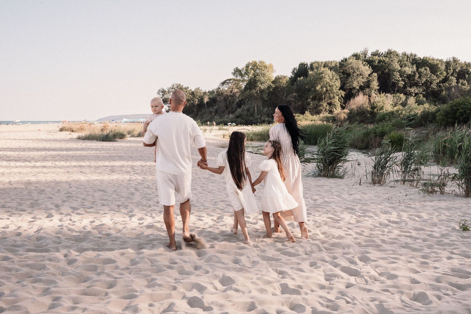 Family members walk hand in hand along sandy beach shore during golden hour.