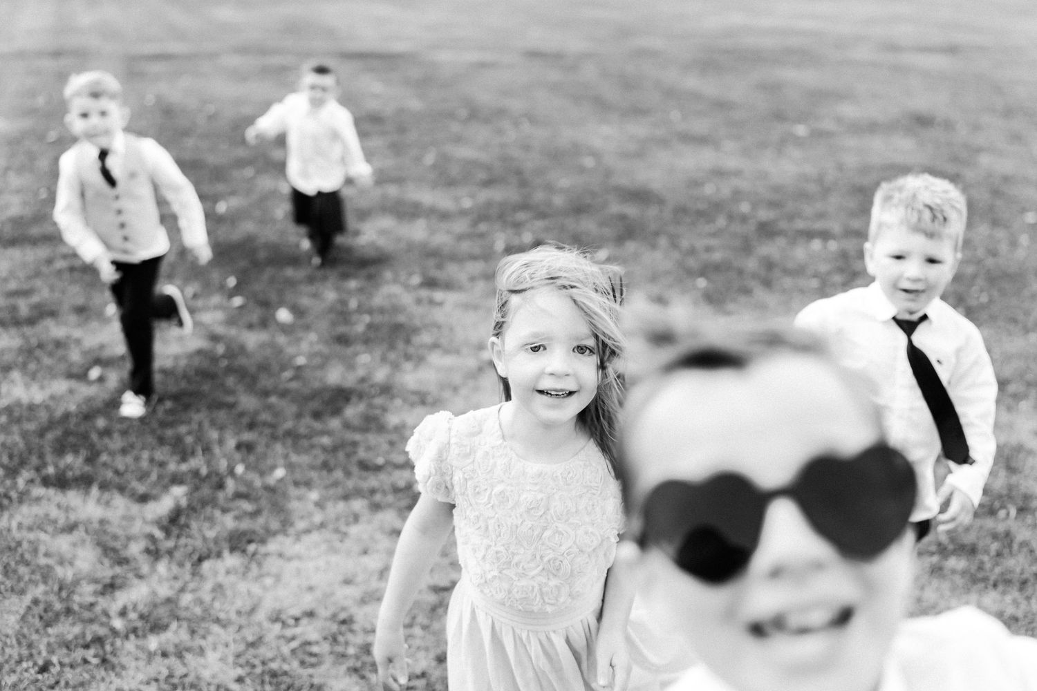 Black and white photo of children running playfully in a field on a sunny day.