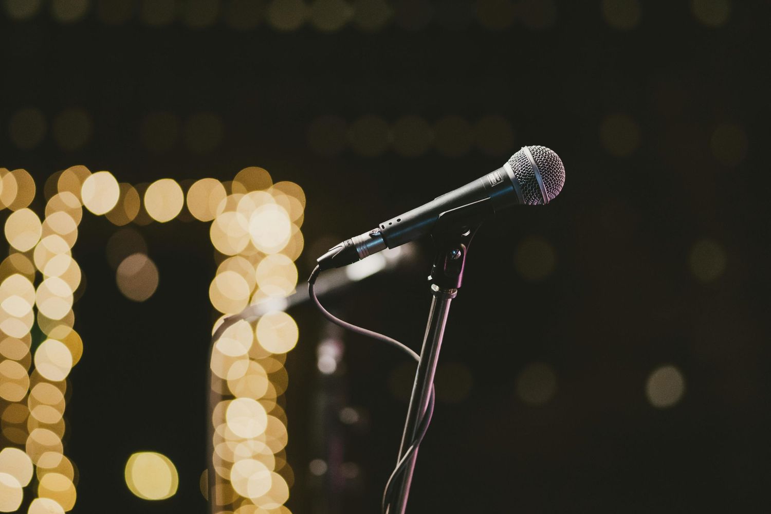 A microphone on a stand positioned against a dark background with blurred golden bokeh lights.