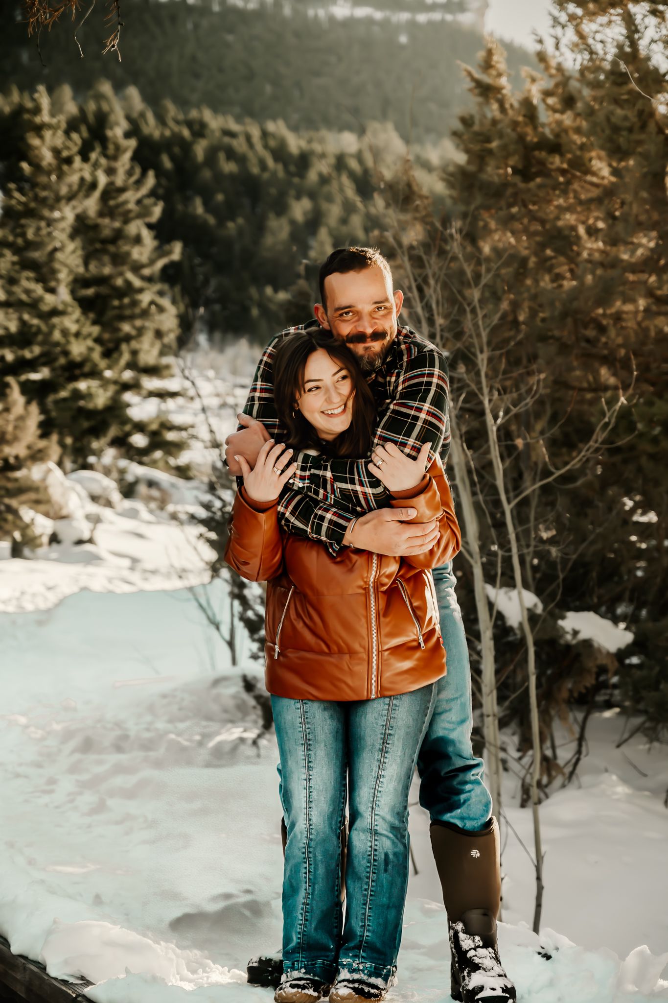 Couple embracing in snowy mountain landscape wearing winter clothing.