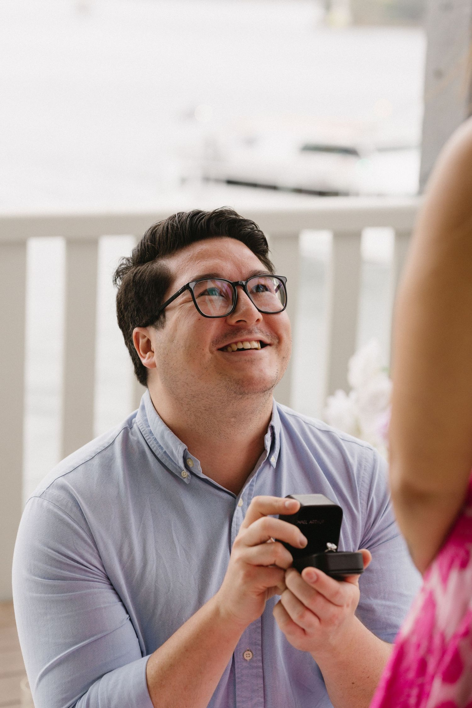 Close-up of joyful moment during proposal with person holding ring box on decorated balcony.