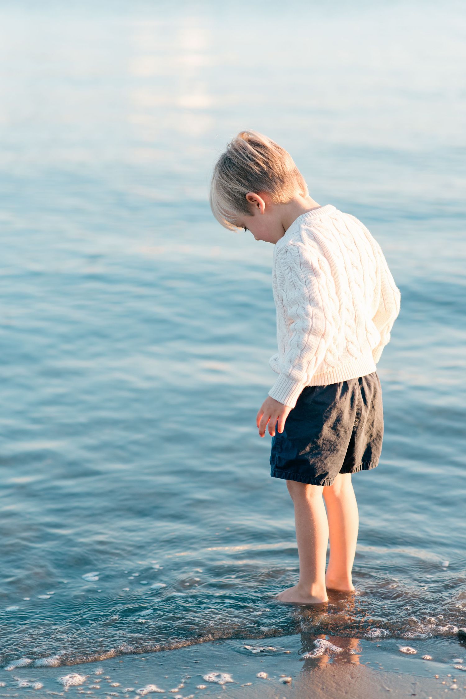 Child playing near the water’s edge at Manasquan Beach, NJ while their parents look on lovingly during a peaceful autumn shoot.