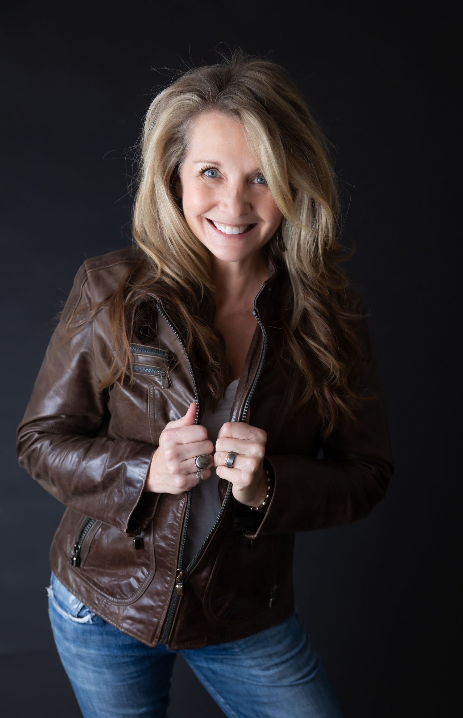 Casual portrait of someone wearing brown leather jacket and jeans with natural smile.