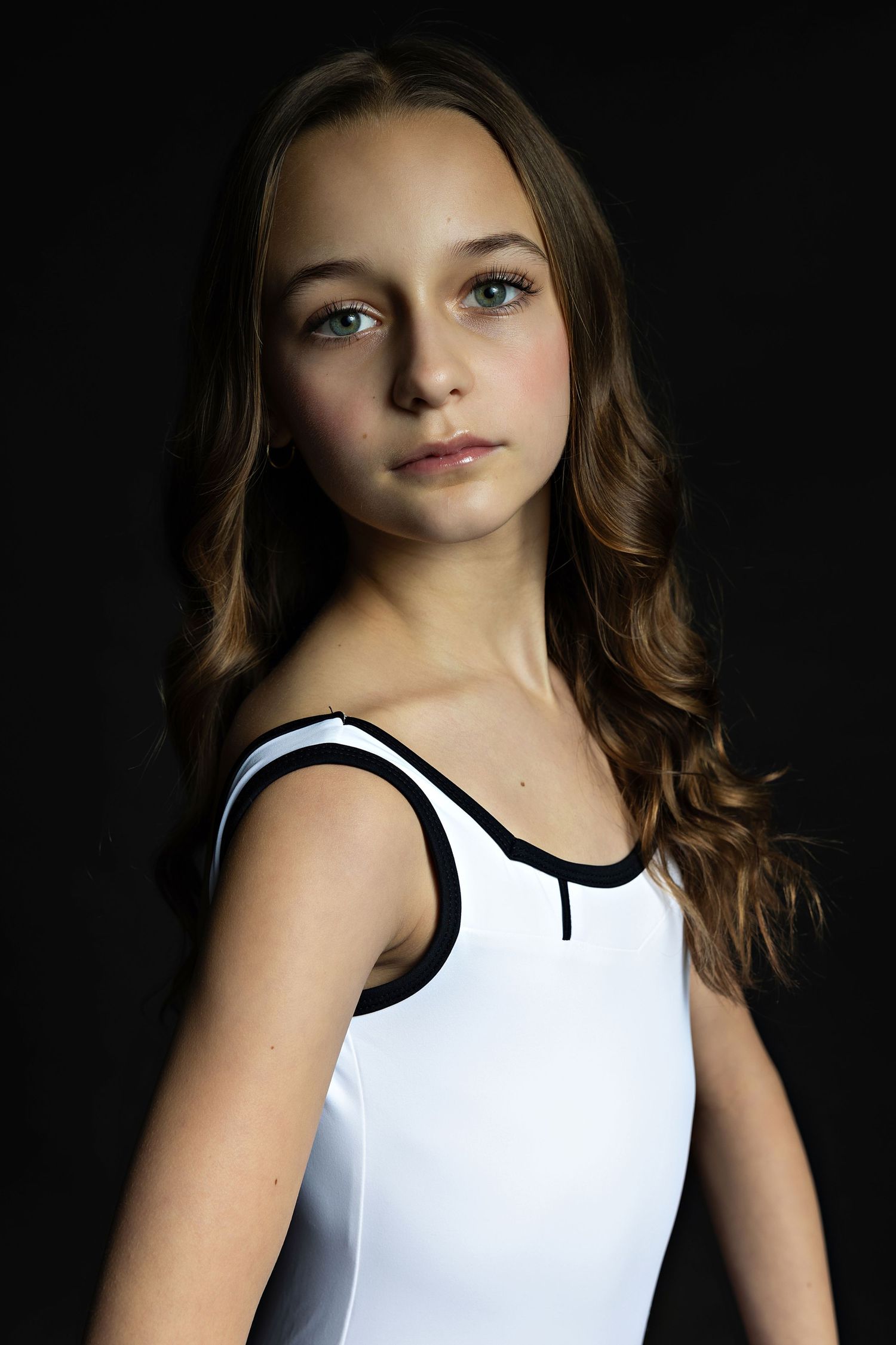 A striking portrait against a dark background features a person wearing a white leotard with black trim.