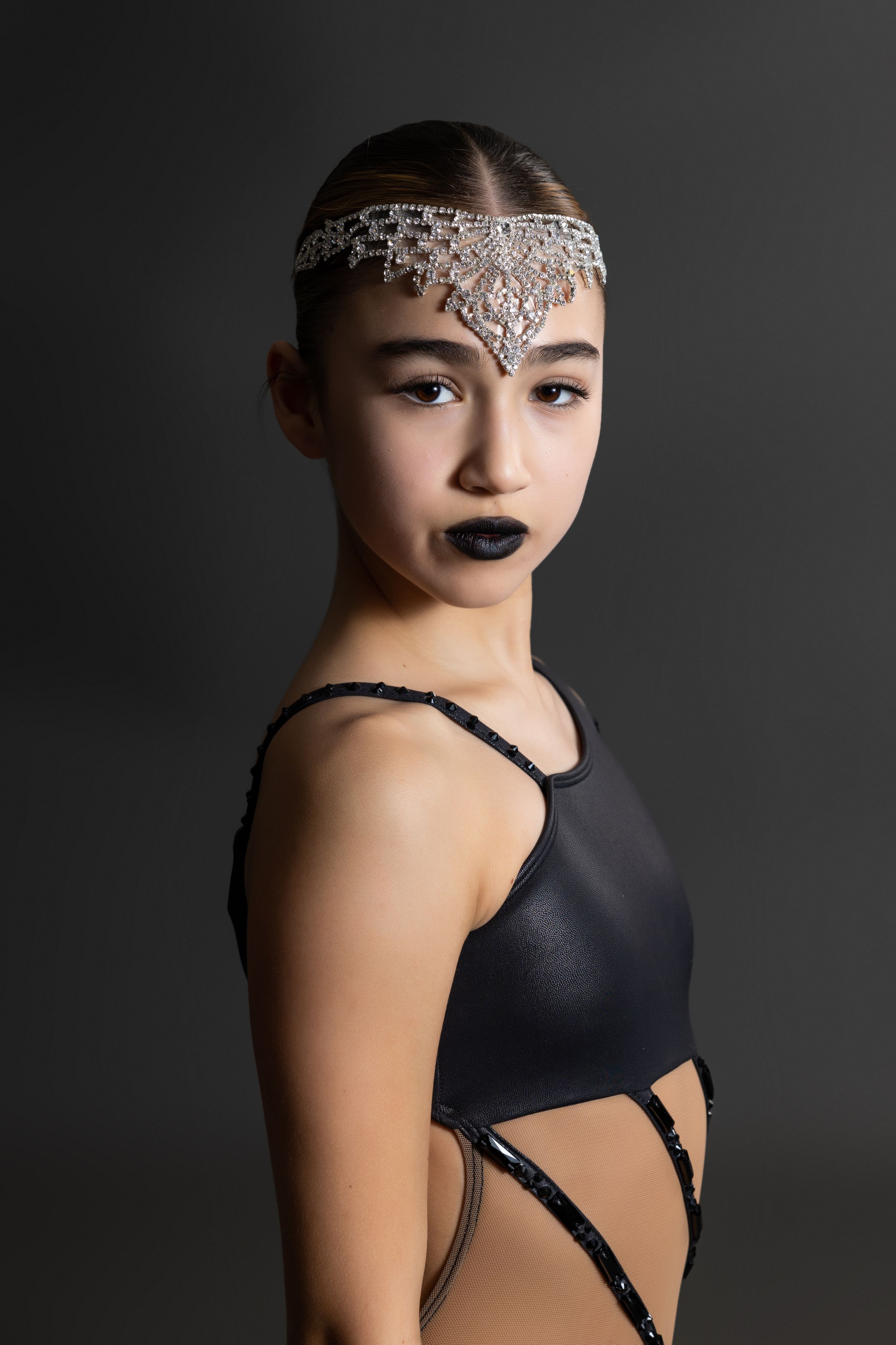 Fashion portrait with intricate rhinestone headpiece and black ballet costume against dark background.
