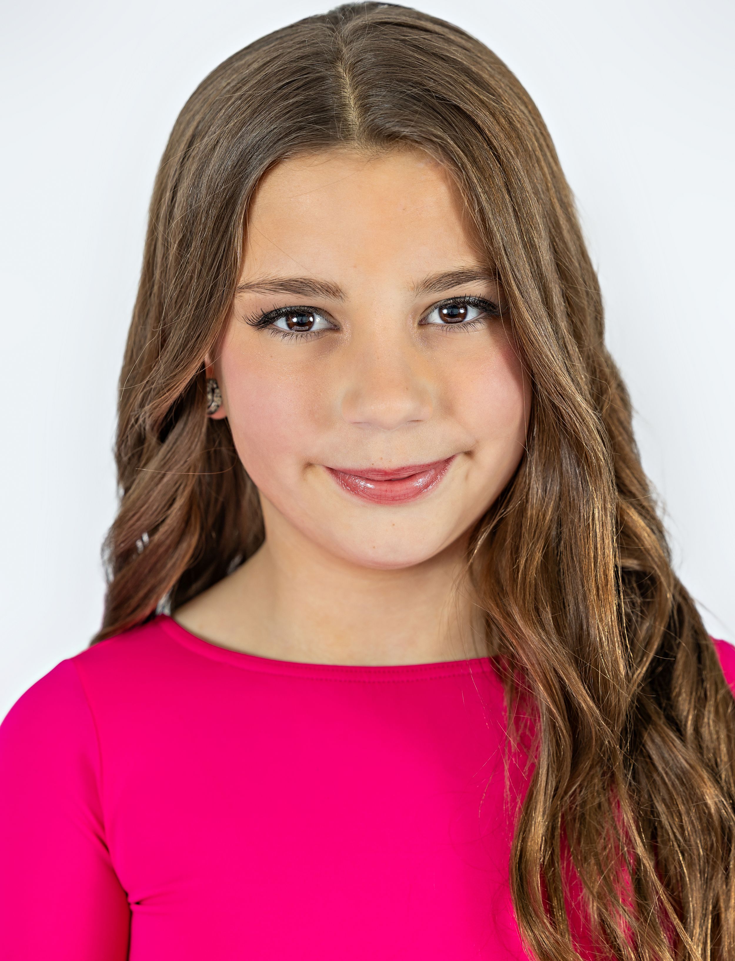 Portrait of someone wearing a bright pink top with long wavy brown hair and a warm smile against a white background.