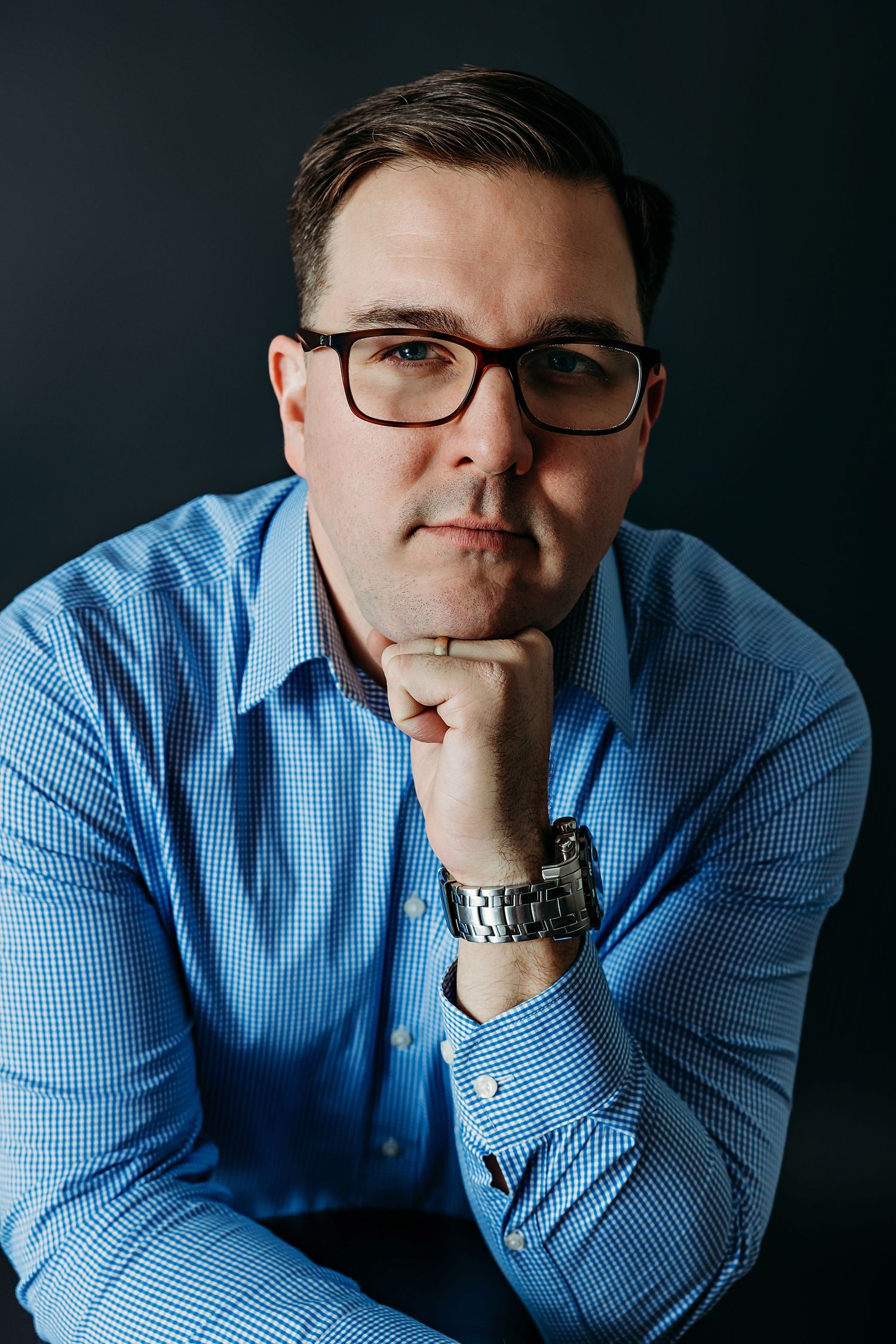 Professional studio portrait of a man in a blue checkered shirt and glasses.