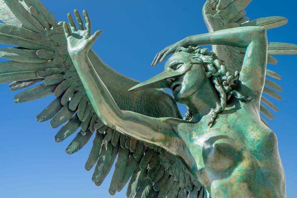 A series of bronze eagle sculptures with outstretched wings soar against a bright blue sky background.