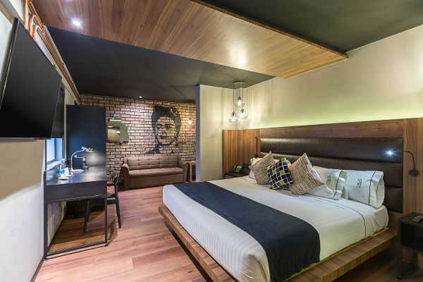 Modern hotel room interior with wooden ceiling, brick accent wall and sleek workstation area. Cadillac Hotel Boutique CDMX.