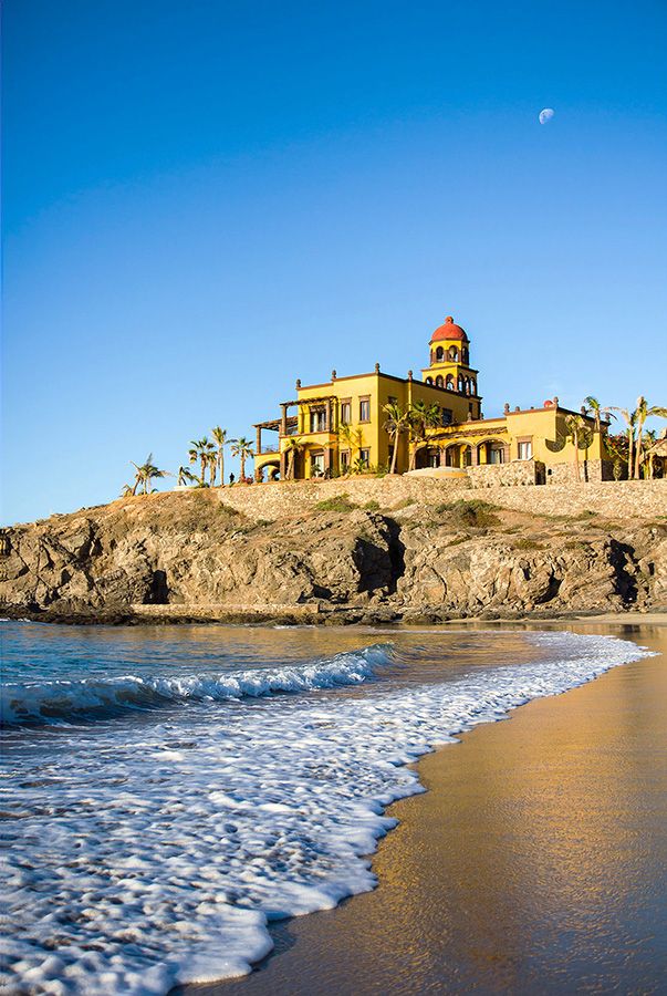 Spanish colonial style mansion perched on rocky cliff above sandy beach. Hacienda Cerritos.