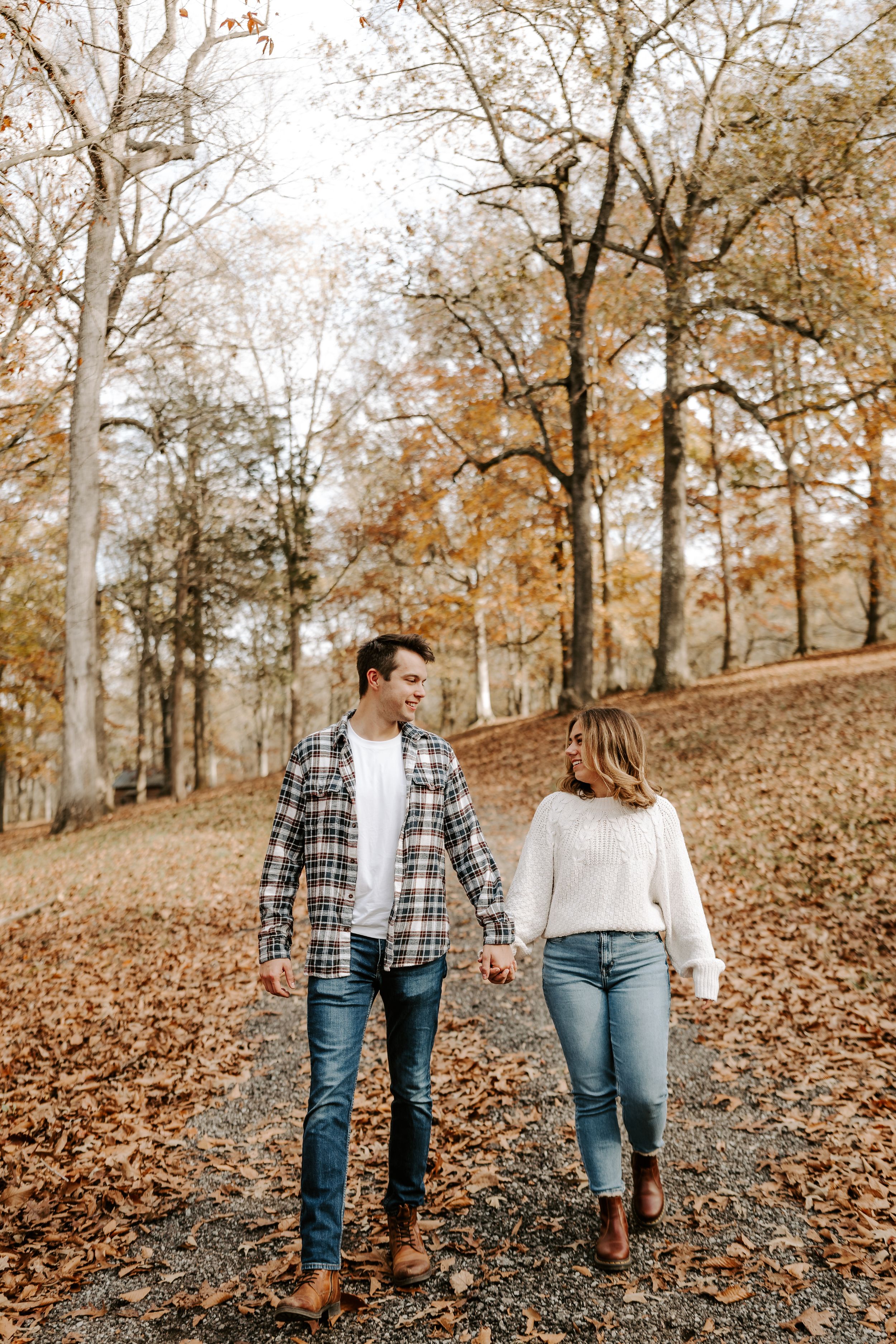 Couple walking through autumn forest with fallen leaves covering the ground.