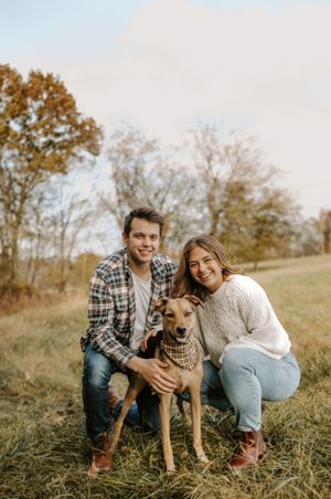 Couple posing with their brown dog in sunny autumn field.