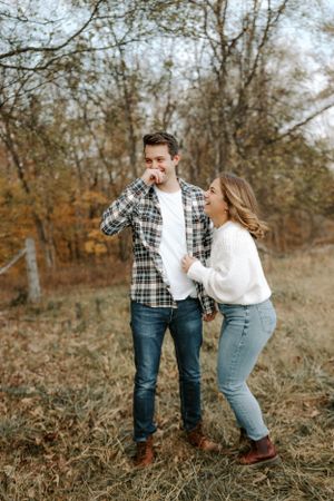 Couple sharing playful moment together in autumn field with fallen leaves.