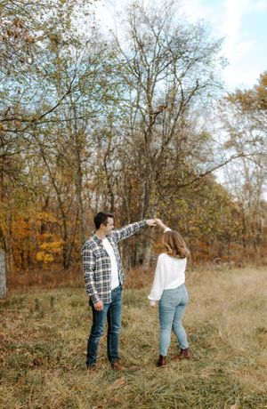 Couple dancing and twirling in autumn field surrounded by trees.