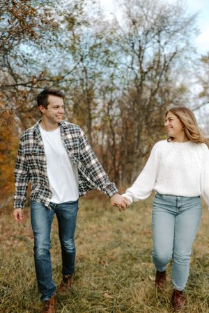 Couple holding hands while walking through autumn field with golden foliage.
