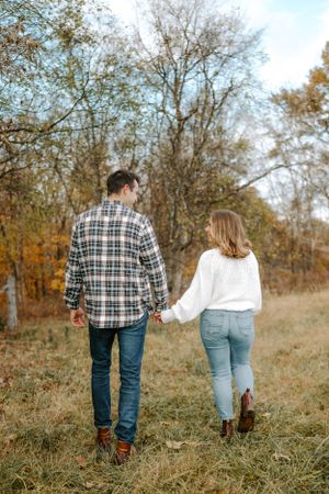 Couple holding hands while walking through a fall meadow wearing coordinated casual outfits.
