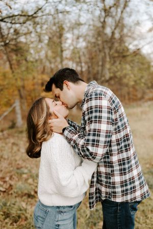 A romantic couple in plaid and white sweaters share tender moments in an autumn field.