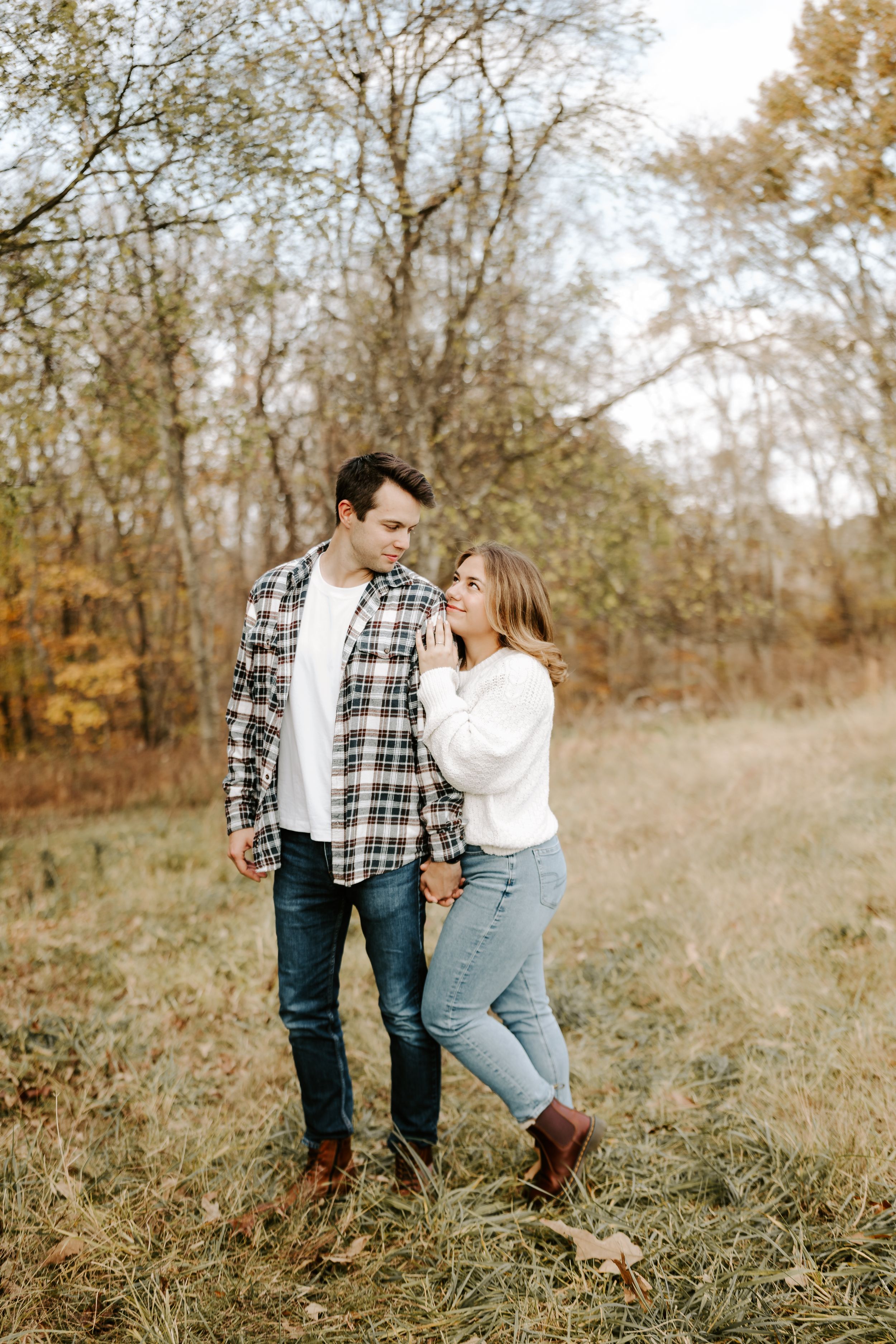 Couple in casual fall attire walking together through tall grass in a natural setting.