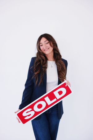 Professional wearing navy blazer holds red SOLD sign in business real estate marketing photo series.