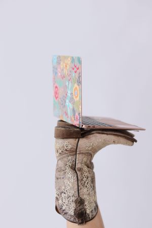A pair of scuffed and weathered boots stacked with floral patterned items balanced on top against a gray background.